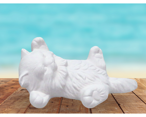 ready to paint ceramic kitten figurine lying on its back on a rustic table near the ocean.  Its feet are sticking out. Its tail is straight.